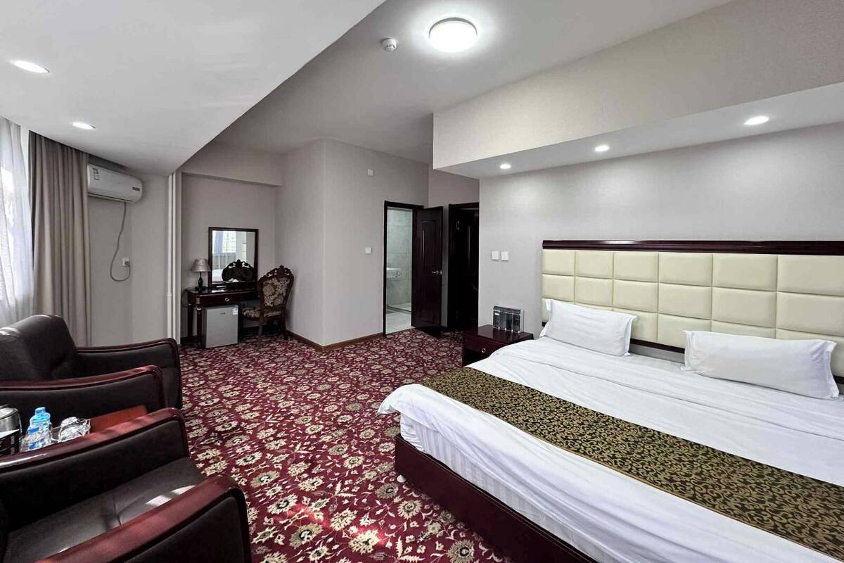 Een hotelkamer met een groot bed, een bureau met stoel, een spiegel en een rode vloerbedekking.
