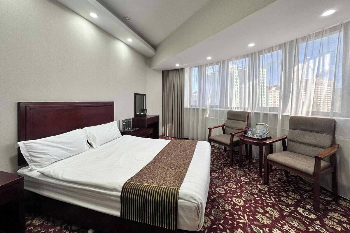 Een hotelkamer met een groot bed, twee fauteuils, een tafeltje en een raam met gordijnen.