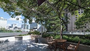An outdoor seating area with tables and chairs, surrounded by greenery and overlooking a cityscape. - Hi Stay Myeongdong (Seoul)