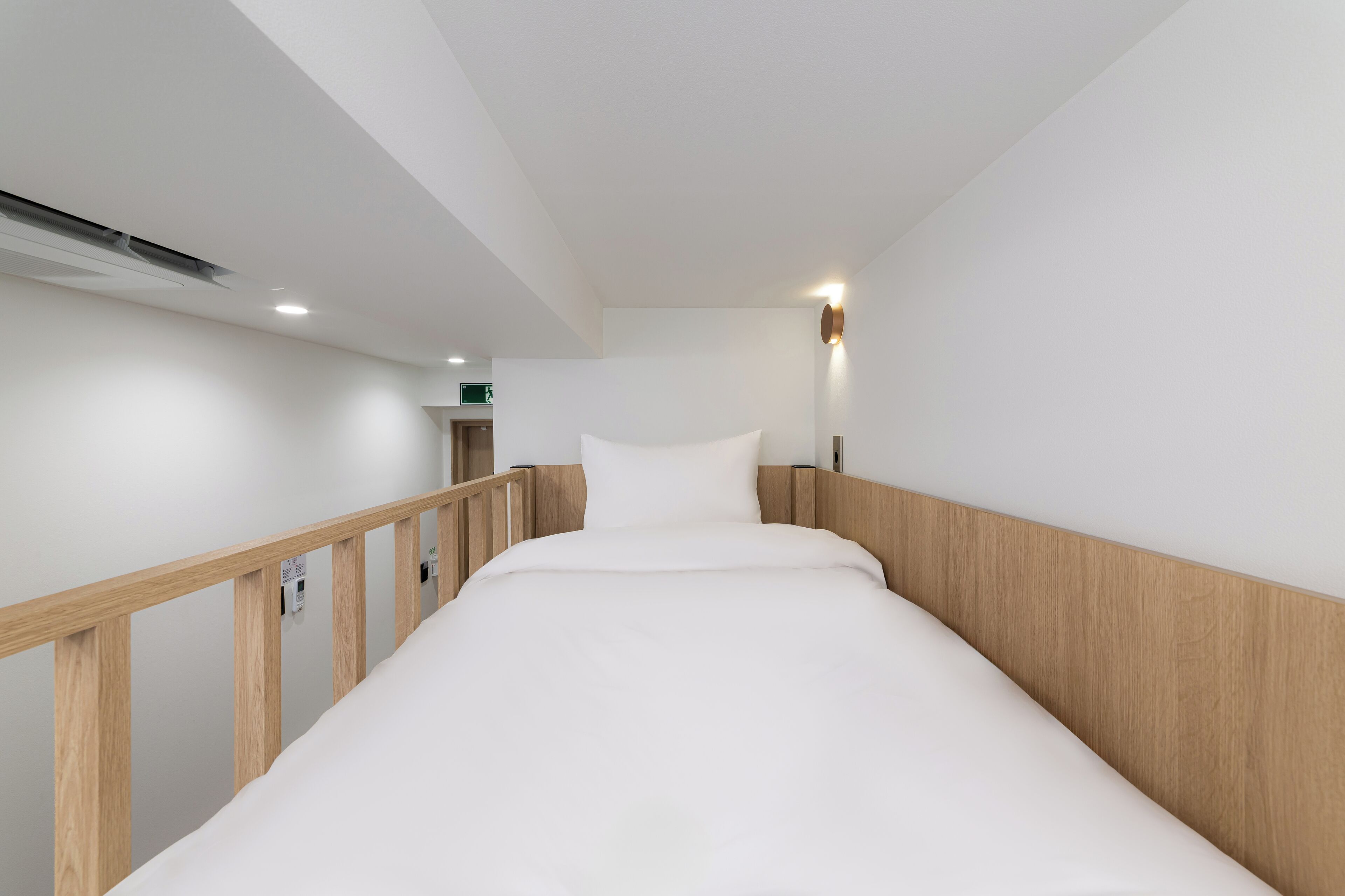 A modern hotel room with a wooden headboard, a white bed, and a small bedside table.