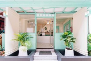 A hotel entrance with a glass door, potted plants, and a ceiling fan. - Catnip Seaside Hotel&Cafe (Phuket)