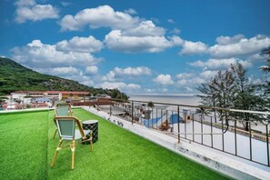 A rooftop terrace with a green lawn, a chair, and a view of a beach and sea. - Catnip Seaside Hotel&Cafe (Phuket)