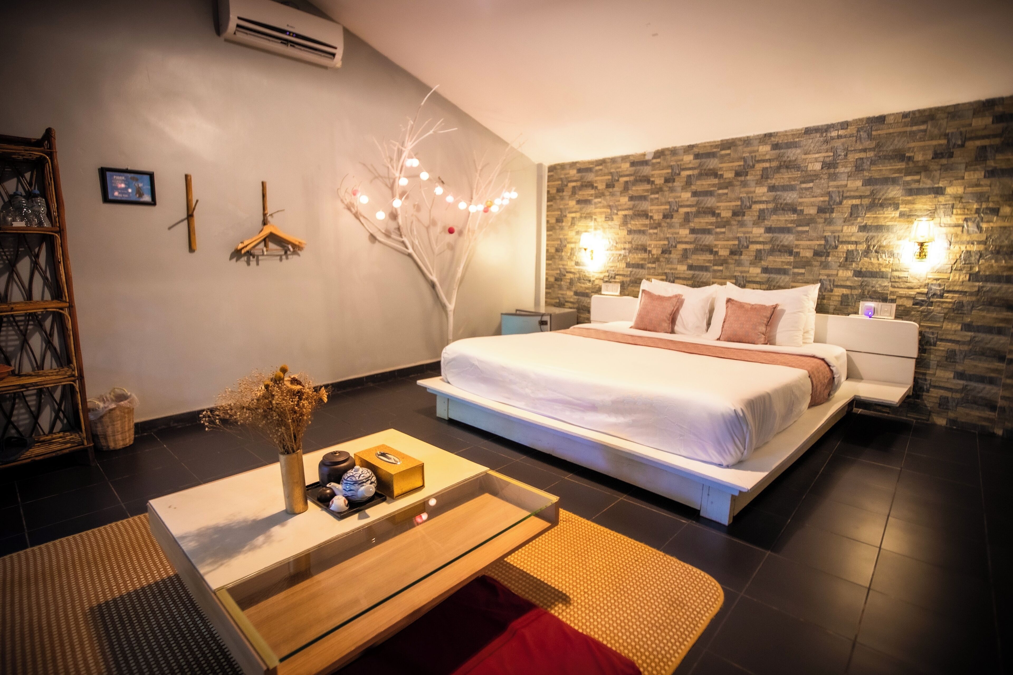 A modern bedroom with a large bed, a bedside table with a vase, a wall-mounted air conditioner, and a textured wall.