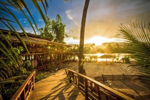 A wooden deck leading to a beach area with thatched-roof structures and palm trees. - Sabay Beach (Kampot)
