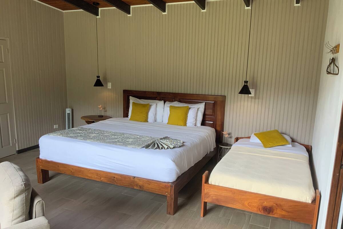 A double bed with a wooden frame and two single beds with wooden frames. There are two bedside tables with lamps, a wall-mounted air conditioner, and a door.