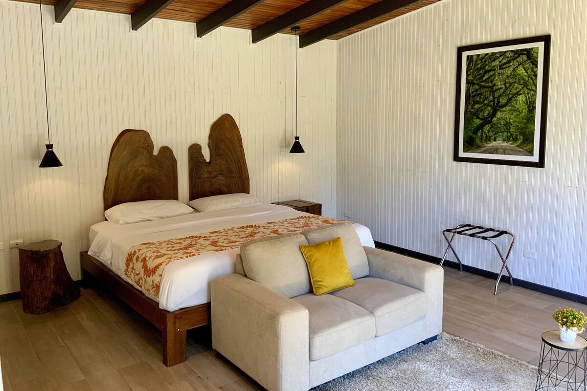 A bedroom with a wooden bed, a sofa, a small table, and a framed picture on the wall.