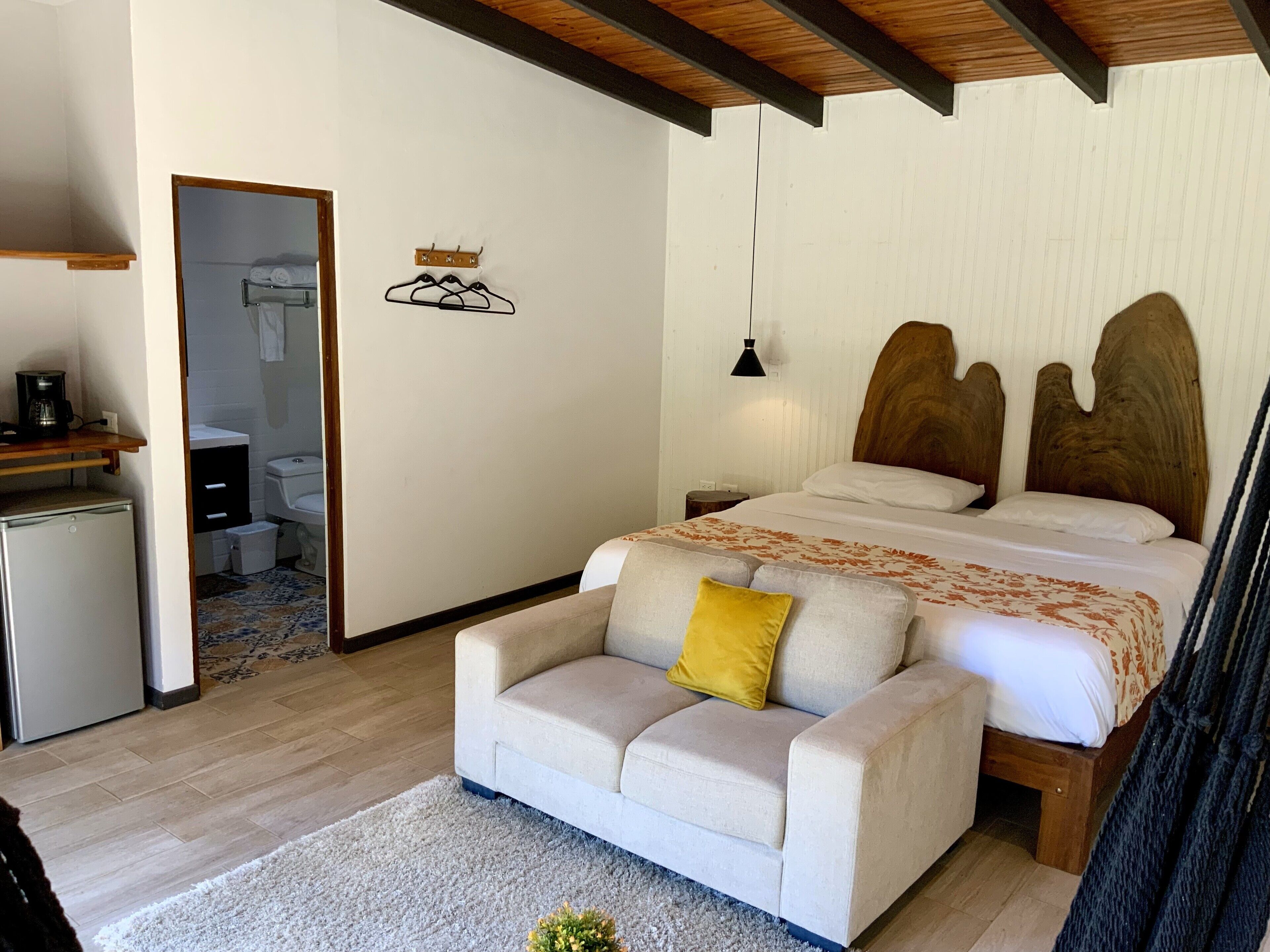 A bedroom with a bed, a sofa, a small desk, a coffee maker, and a bathroom visible through an open door.