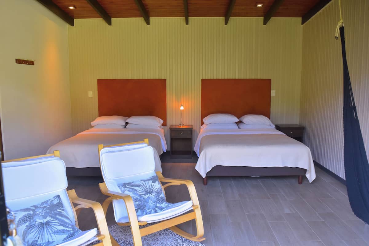 A hotel room with two beds, wooden chairs, a nightstand, and a hanging hammock.