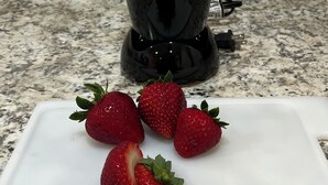 Una cocina con una licuadora en la encimera, una tabla de cortar blanca con fresas, y un enchufe de corriente al fondo.