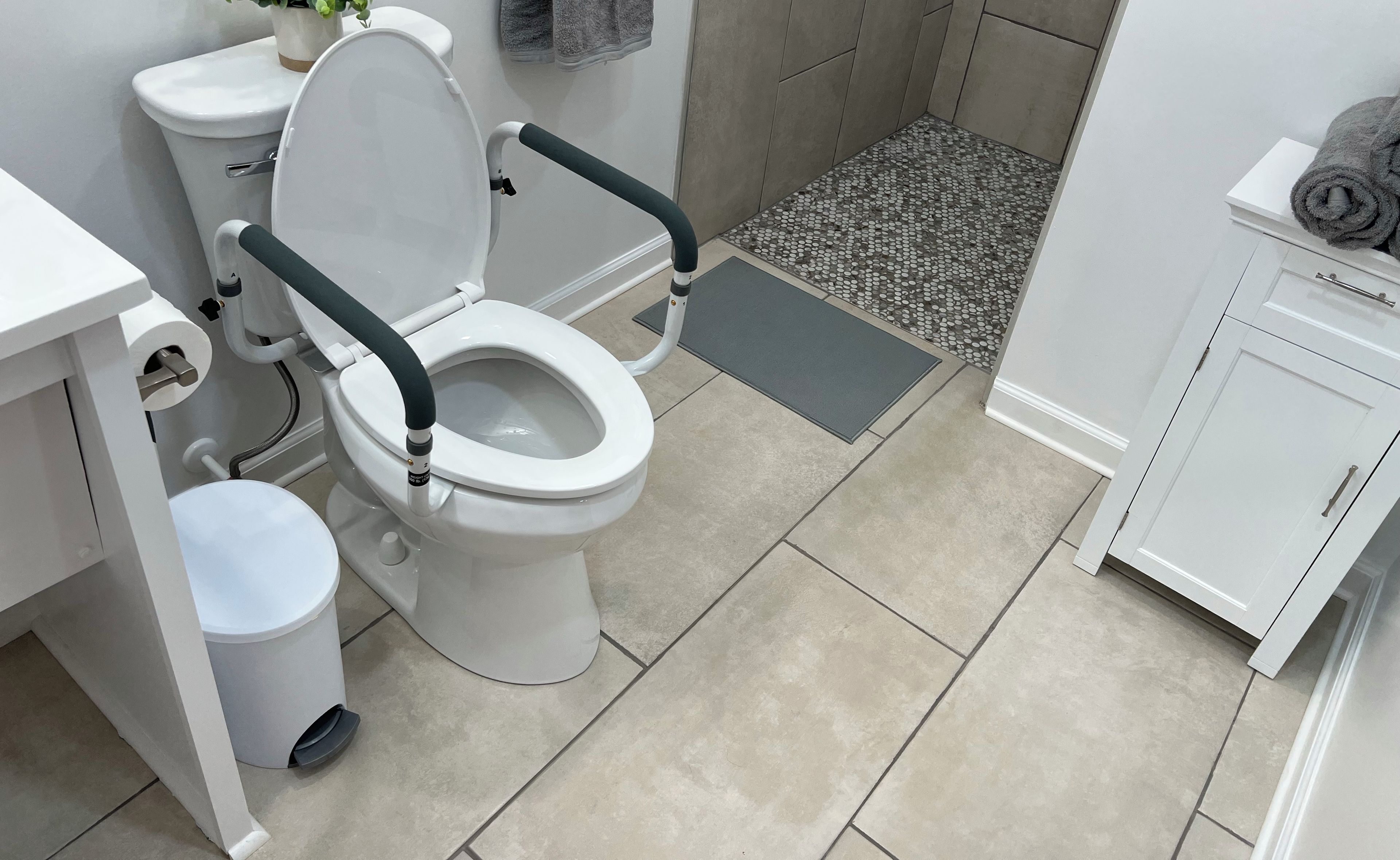 A modern bathroom with a white toilet, a small potted plant, and a grey towel on a cabinet.