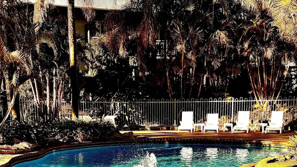 Una piscina con fuente de agua, rodeada de palmeras y sillas de descanso.