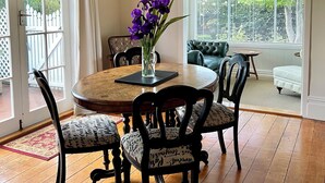 A dining area with a round table, four chairs, a chandelier, and a view of the outdoors through large windows.