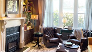 A traditional living room with a fireplace, leather armchairs, a patterned rug, and a chandelier.