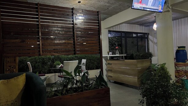 A lobby with a reception desk, seating area, and a television mounted on the wall. - Sophie's Garden Hotel Kapenguria (Makutano)