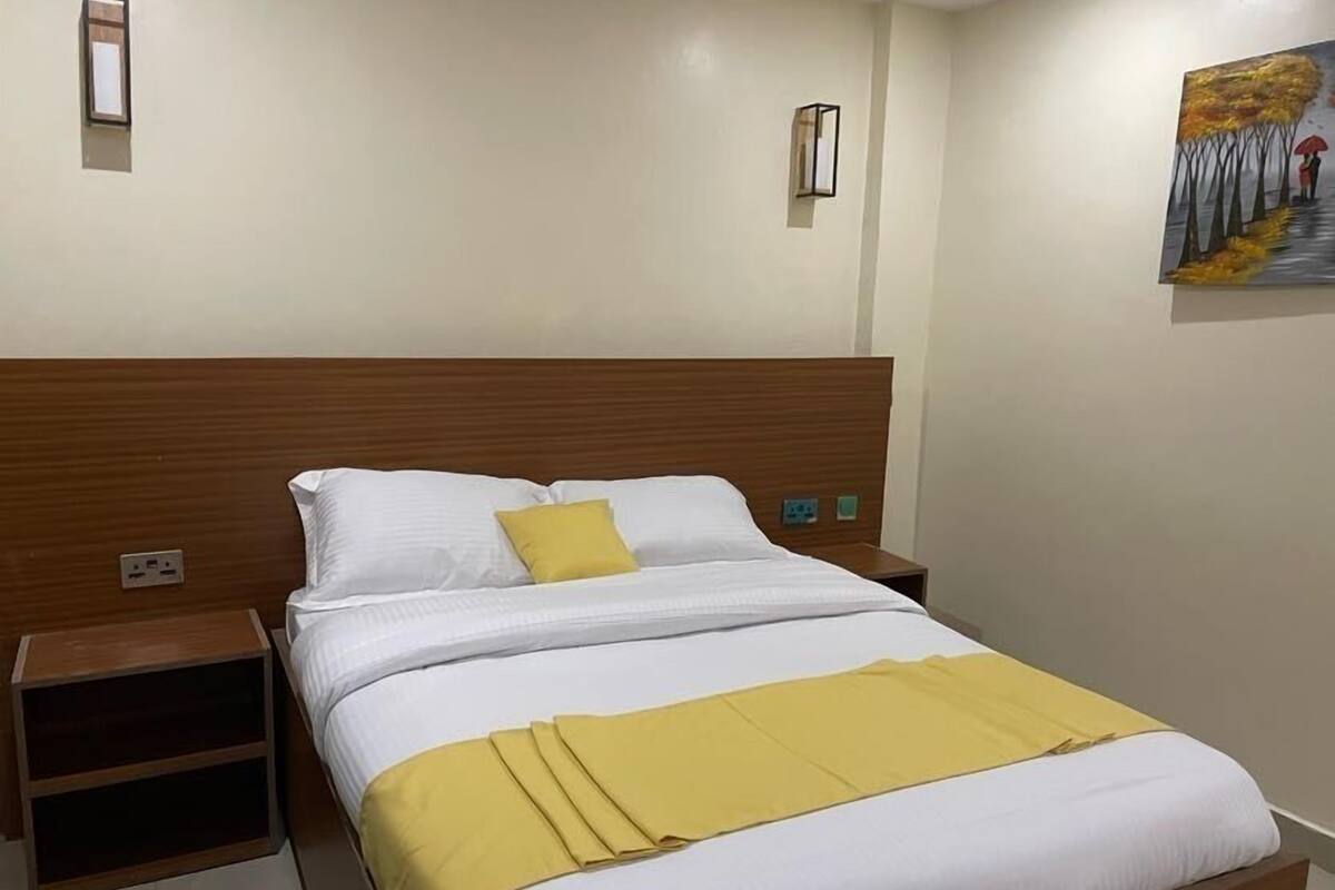 A neatly made bed with white and yellow bedding, a wooden headboard, and bedside tables with lamps.
