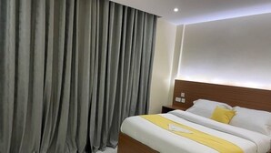 A hotel room with a large bed, a wooden headboard, a nightstand, and grey curtains. - Sophie's Garden Hotel Kapenguria (Makutano)