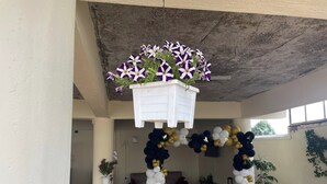 An outdoor dining area with a table set for two, surrounded by white chairs, and a hanging planter with flowers above. - Sophie's Garden Hotel Kapenguria (Makutano)
