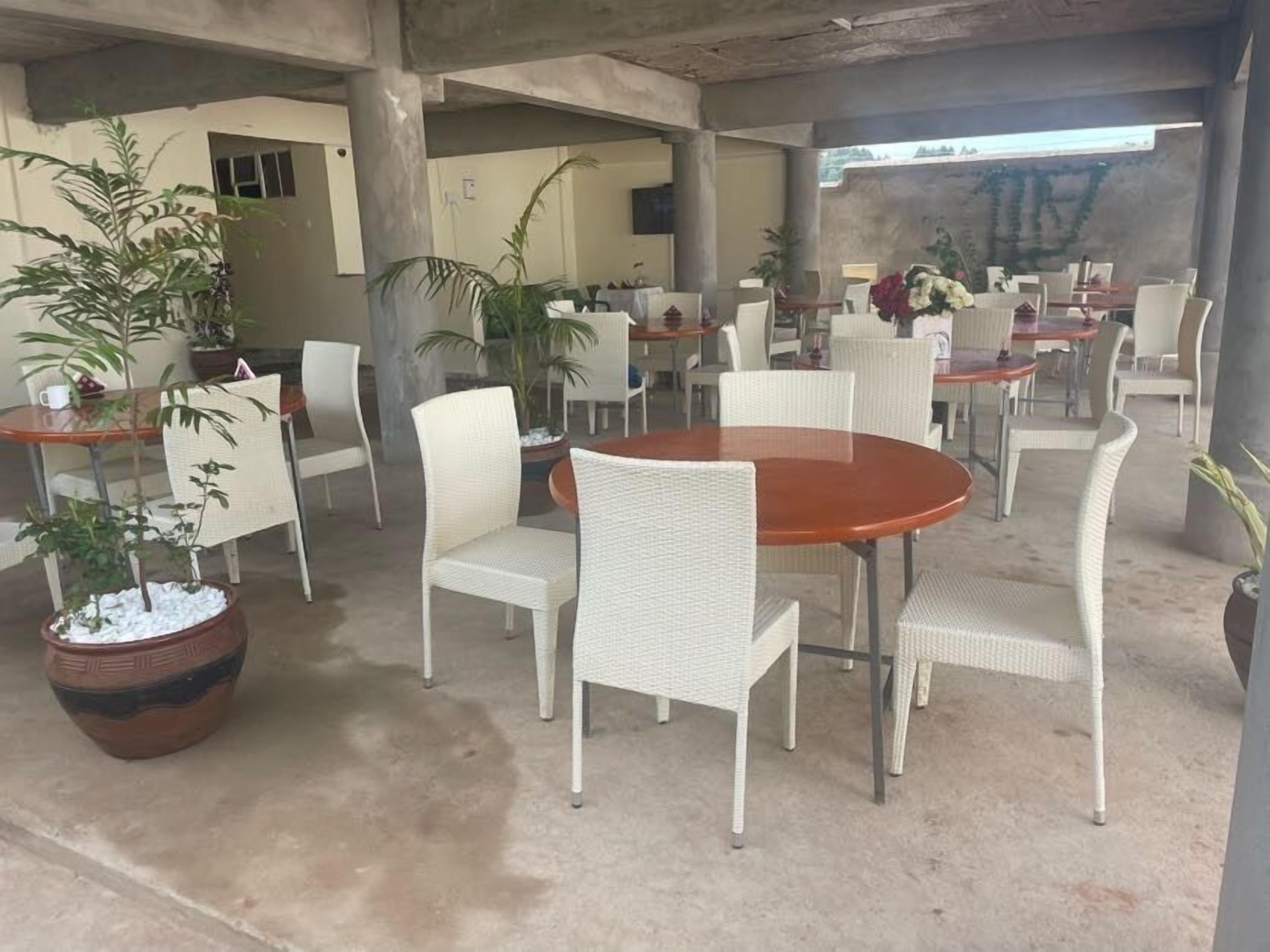 An outdoor seating area with white wicker chairs and tables, surrounded by potted plants.