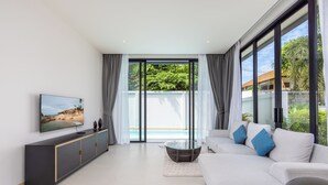 A modern living room with a large TV, a sofa, and a glass coffee table. - Villa Noa  Modern 2BR with Private Pool (Rawai)