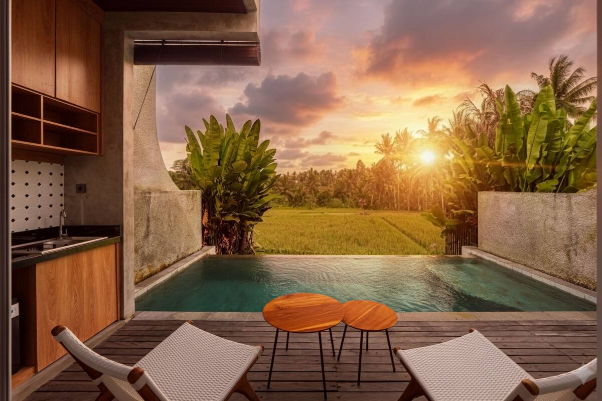 An outdoor pool area with two lounge chairs and a small table, surrounded by tropical plants and a view of a lush landscape.