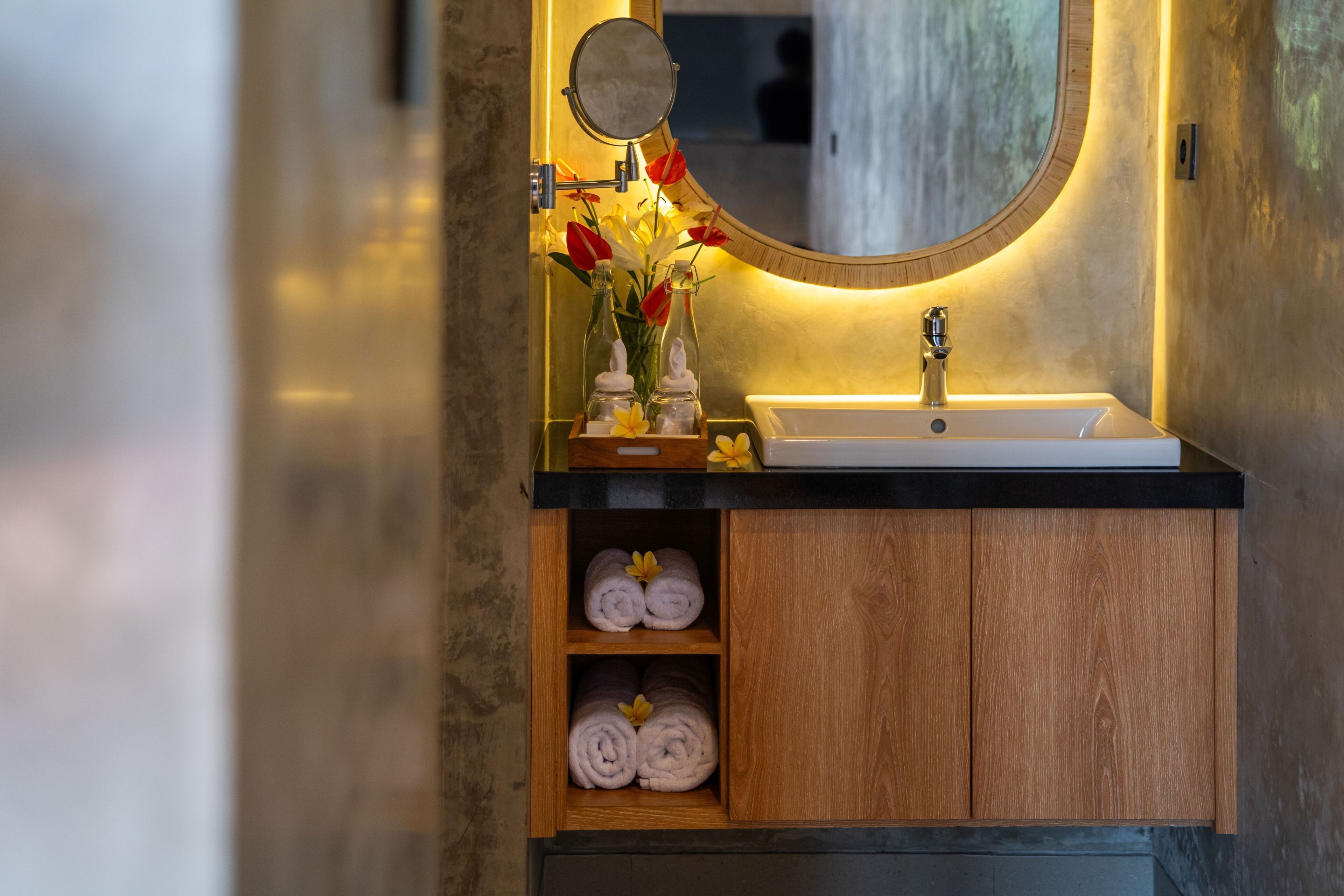 A bathroom with a wooden vanity, a mirror, a sink, and a shelf with towels.