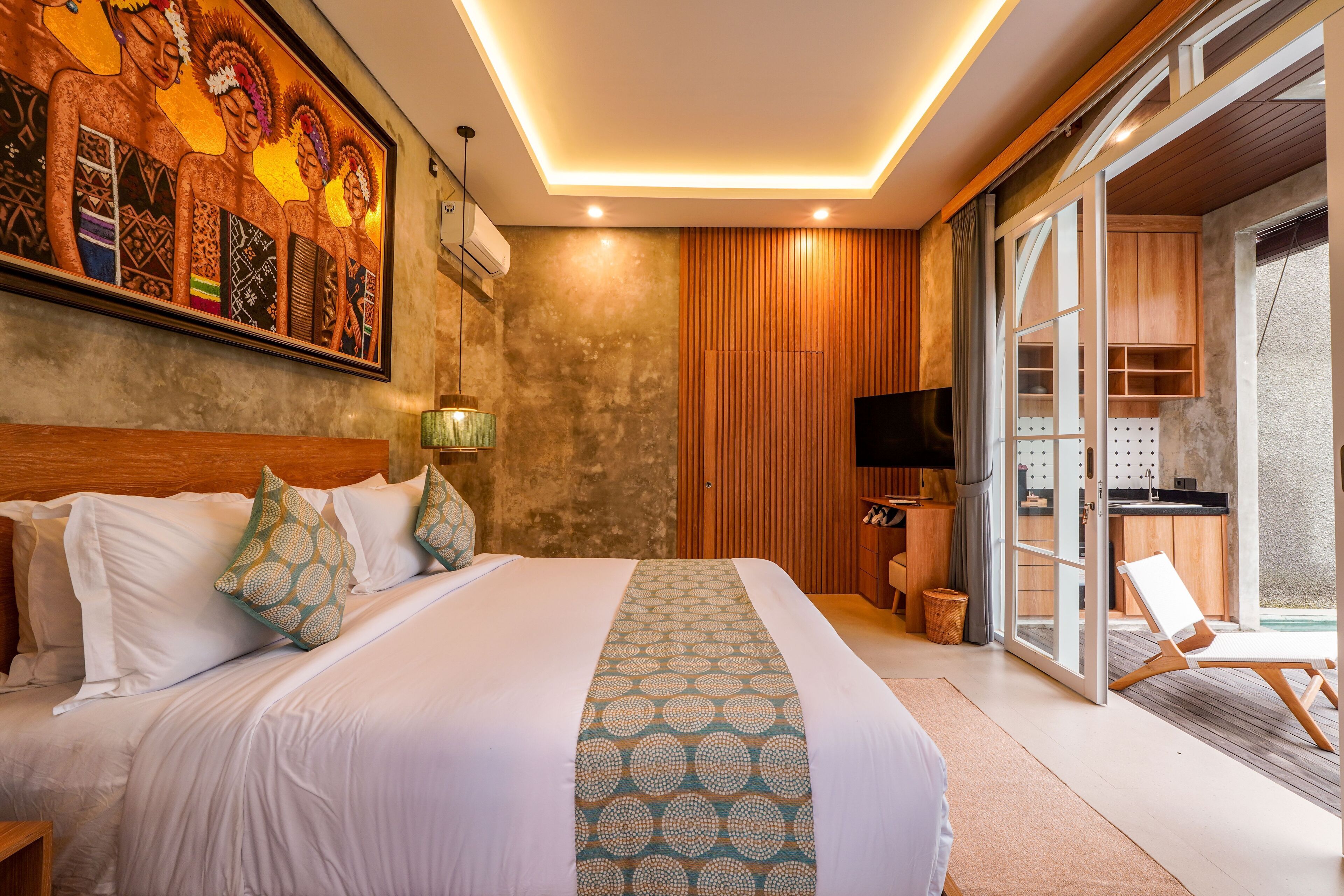 Habitación de hotel con una cama grande, un cuadro en la pared, un televisor y una puerta corrediza de cristal que da a un balcón.