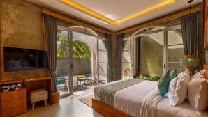 A bedroom with a large bed, a TV, a wooden desk, and a sliding glass door leading to an outdoor area. - Subu Utamas Villas (Payangan)