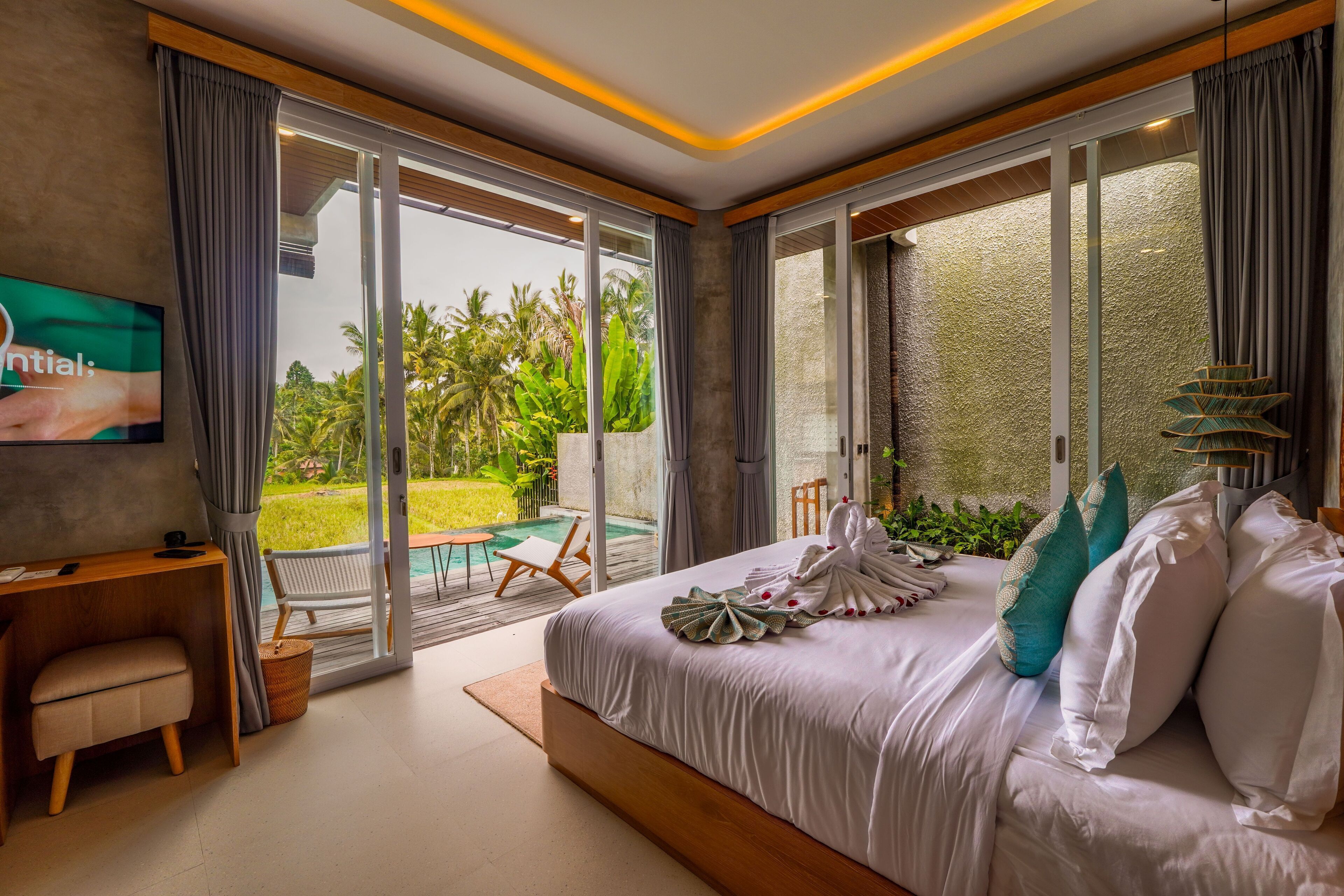 Un dormitorio con cama, escritorio, silla, televisor y vistas a una piscina y jardín.