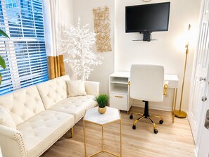A modern living room with a sofa, a small table, a desk, and a TV mounted on the wall.