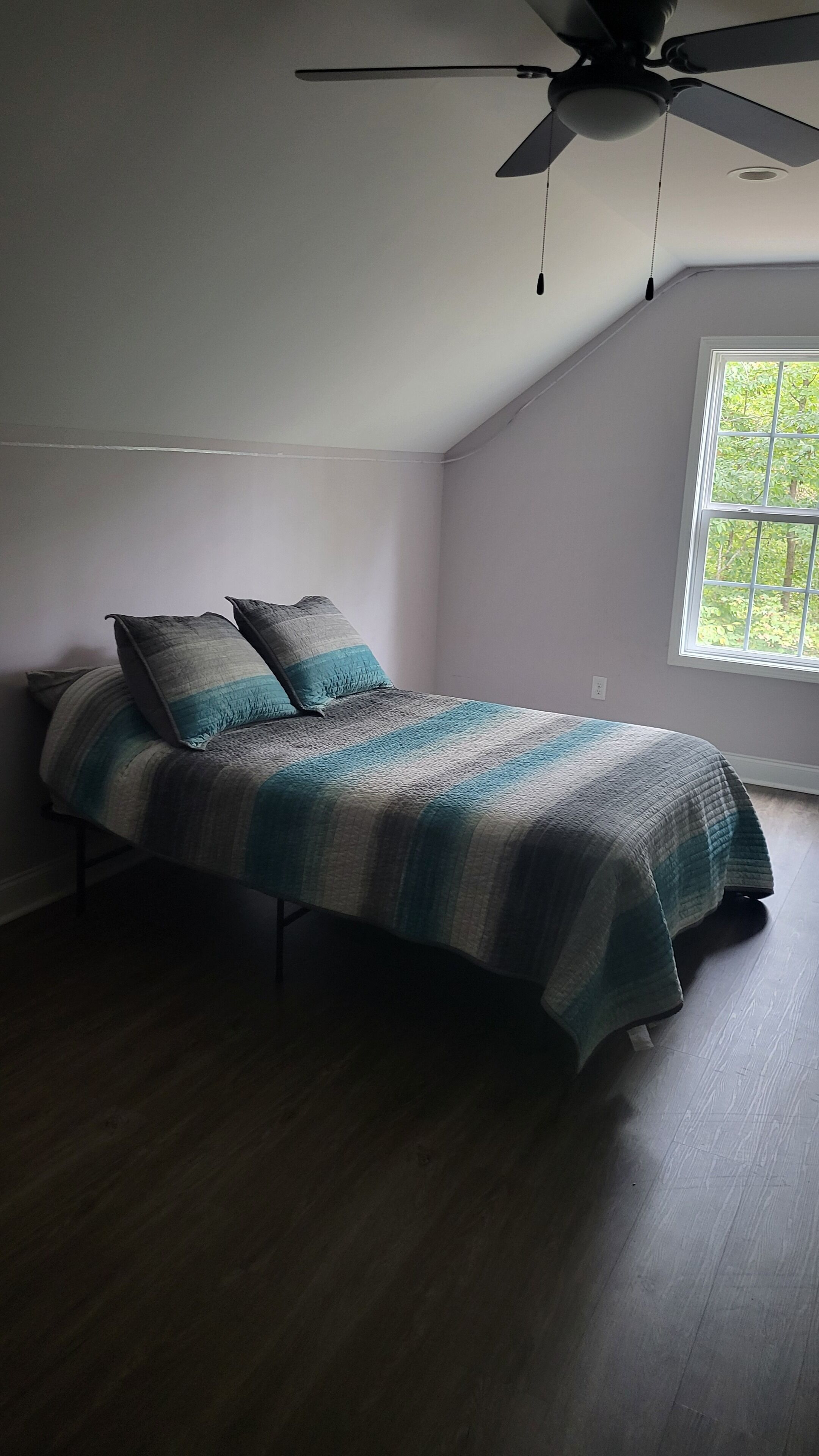A bedroom with a bed, a ceiling fan, and a window with a view of greenery.