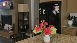 Una cocina con encimeras de granito, una isla central con un florero, iluminación colgante y un refrigerador con imanes.