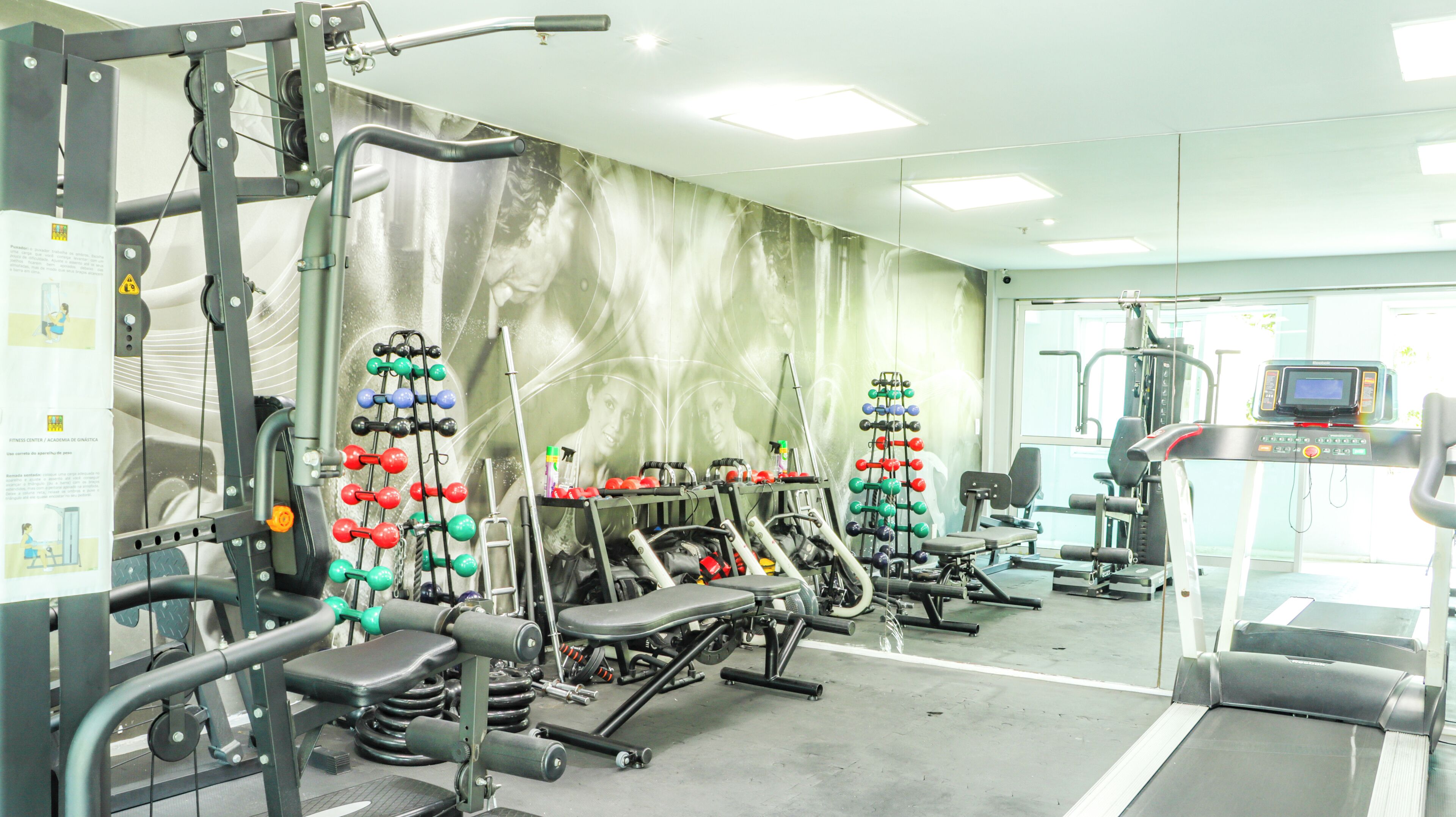 Een sportschool met diverse fitnessapparaten, een muur met een muurschildering en een loopband.