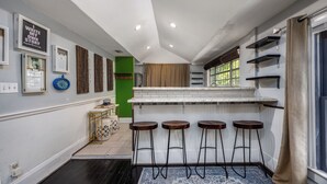 A kitchen with a bar area, stools, and a green accent wall. - Luxury Retreat Just Steps from UF Main Campus (Gainesville)