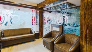 A lobby with a sofa and armchairs, a decorative glass wall, and a chandelier. - Hotel Saad (Kolkata)