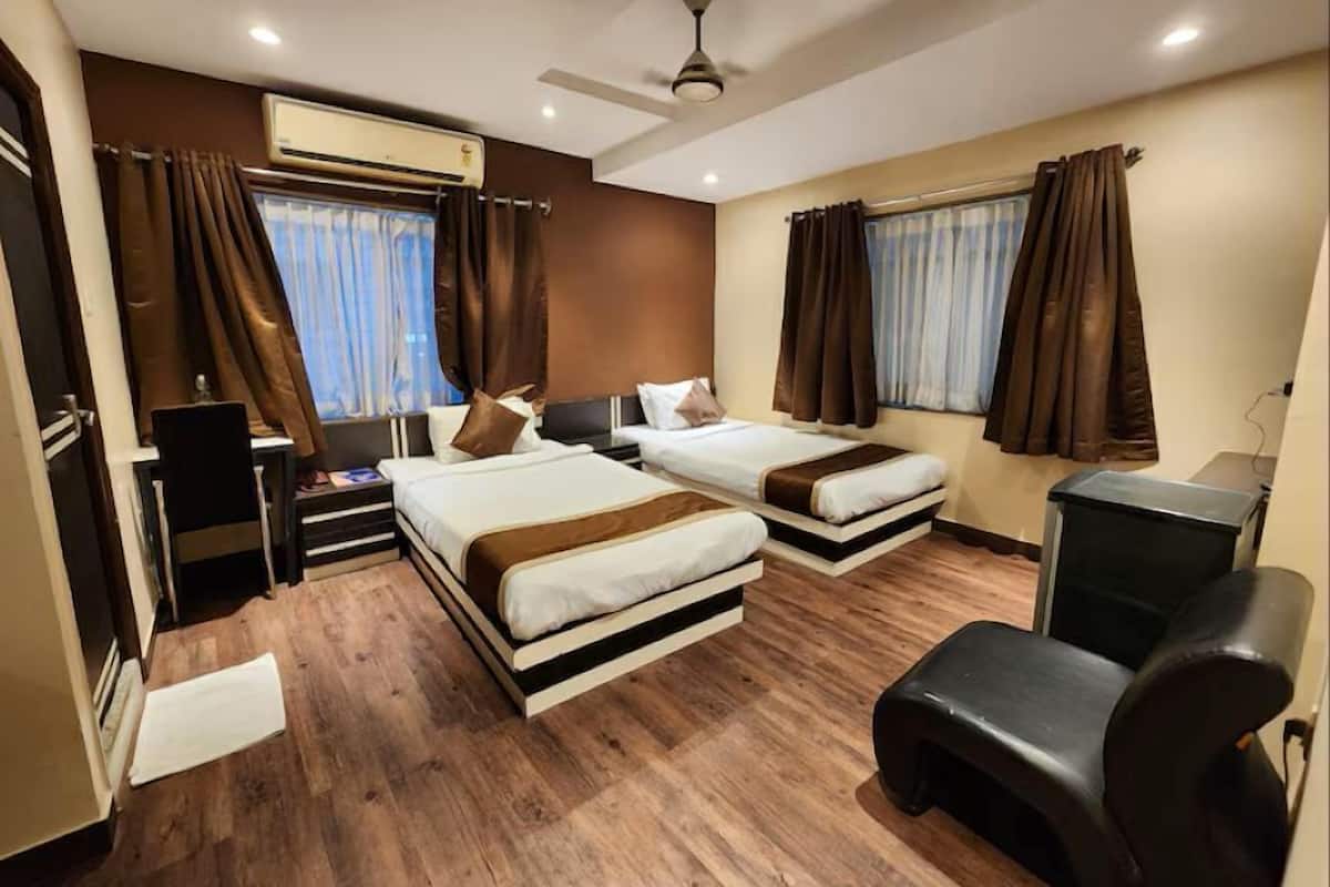 A hotel room with two beds, a desk, a chair, an air conditioning unit, and a ceiling fan.