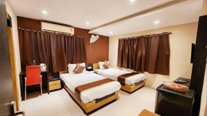 A hotel room with two beds, a desk, a chair, a TV, and a small table with a basket. - Hotel Saad (Kolkata)