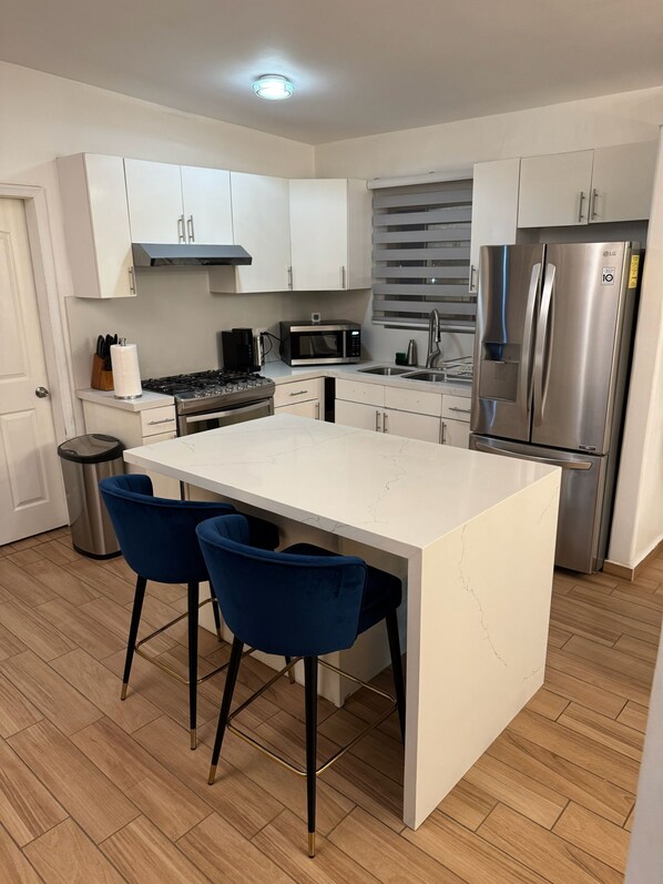 A modern kitchen with white cabinets, stainless steel appliances, a central island with bar stools, and a wooden floor.