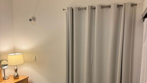 A bedroom with a bed, a bedside table with a lamp, a mirror, and an air conditioning unit mounted on the wall.