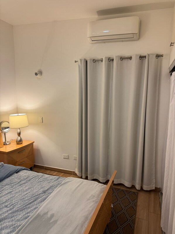 Un dormitorio con cama, mesita de noche con lámpara, espejo y unidad de aire acondicionado en la pared.