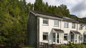 A two-story house with a stone facade, multiple windows, and a small porch area. - 22 Thrang Brow -  3 Bedroom Holiday Home - Langdale Valley (Chapel Stile)