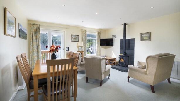 A cozy living room with a wooden dining table, two armchairs, and a fireplace. - 22 Thrang Brow -  3 Bedroom Holiday Home - Langdale Valley (Chapel Stile)