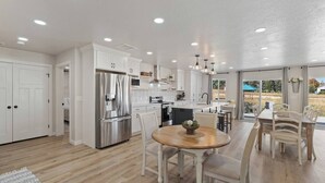 Una cocina moderna con muebles blancos, electrodomésticos de acero inoxidable y una zona de comedor con una mesa redonda y sillas.