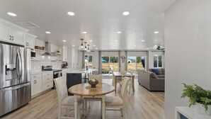 Una cocina moderna con armarios blancos, un refrigerador de acero inoxidable y un comedor con una mesa redonda de madera y sillas.