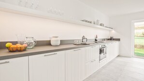 Eine moderne Küche mit weißen Schränken, einer Arbeitsfläche mit Küchenutensilien und Blick ins Freie.