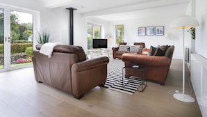 Ein modernes Wohnzimmer mit zwei Ledersofas, einem Flachbildfernseher und einem großen Fenster mit Blick auf den Garten.