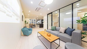A modern living room with a sofa, a coffee table, and a blue armchair. There is a kitchen area in the background with a dining table and chairs. - STARRY STAY HOUSE SHIBUYA I (Tokyo)