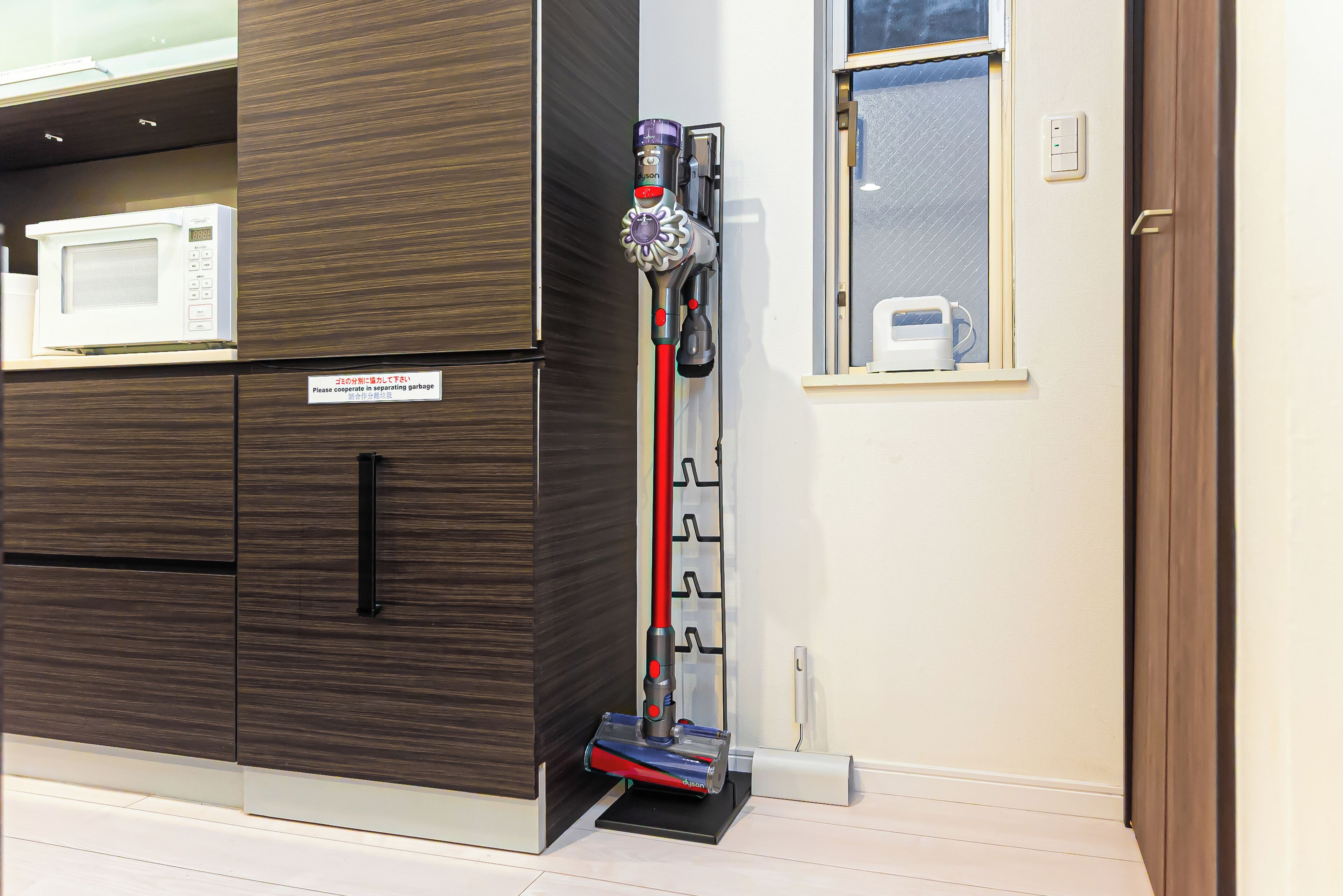A kitchen area with a microwave, cabinets, and a Dyson vacuum cleaner.