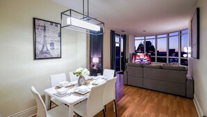 Ett modernt vardagsrum med en matplats, en soffa och en tv-skärm som visar en stadsbild.