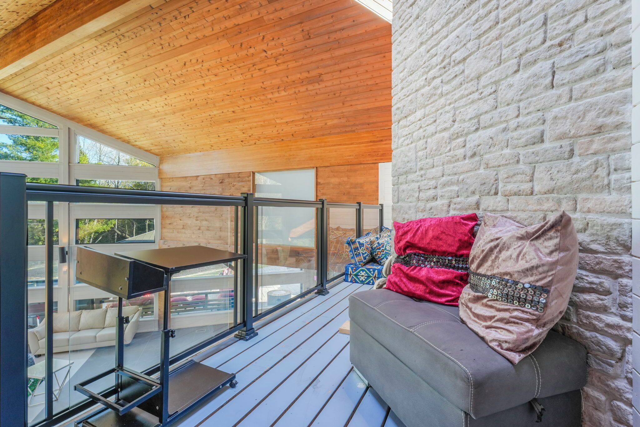 Un espace extérieur moderne, aménagé avec un plafond en bois, un mur en pierre et une rambarde en verre.