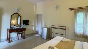 A hotel room with a bed, a desk, a television, a ceiling fan, and a window with curtains. - The Grand Oak By TERASTAY (Virajpet)